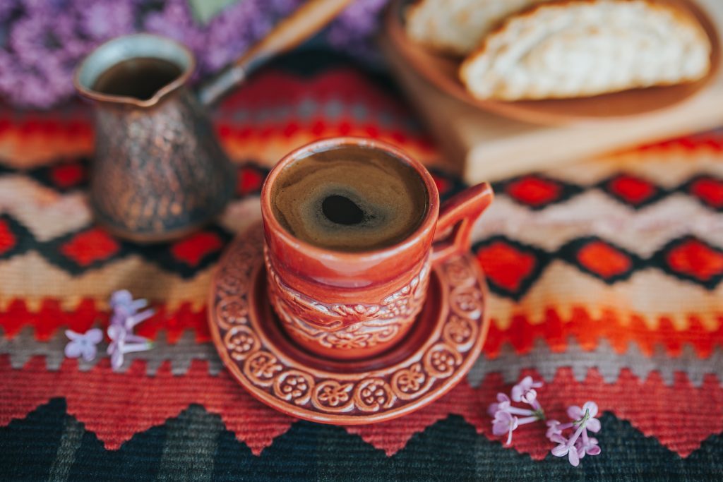 Armenian coffee in a red ceramic cup and saucer beside a copper jezve on a traditional woven rug